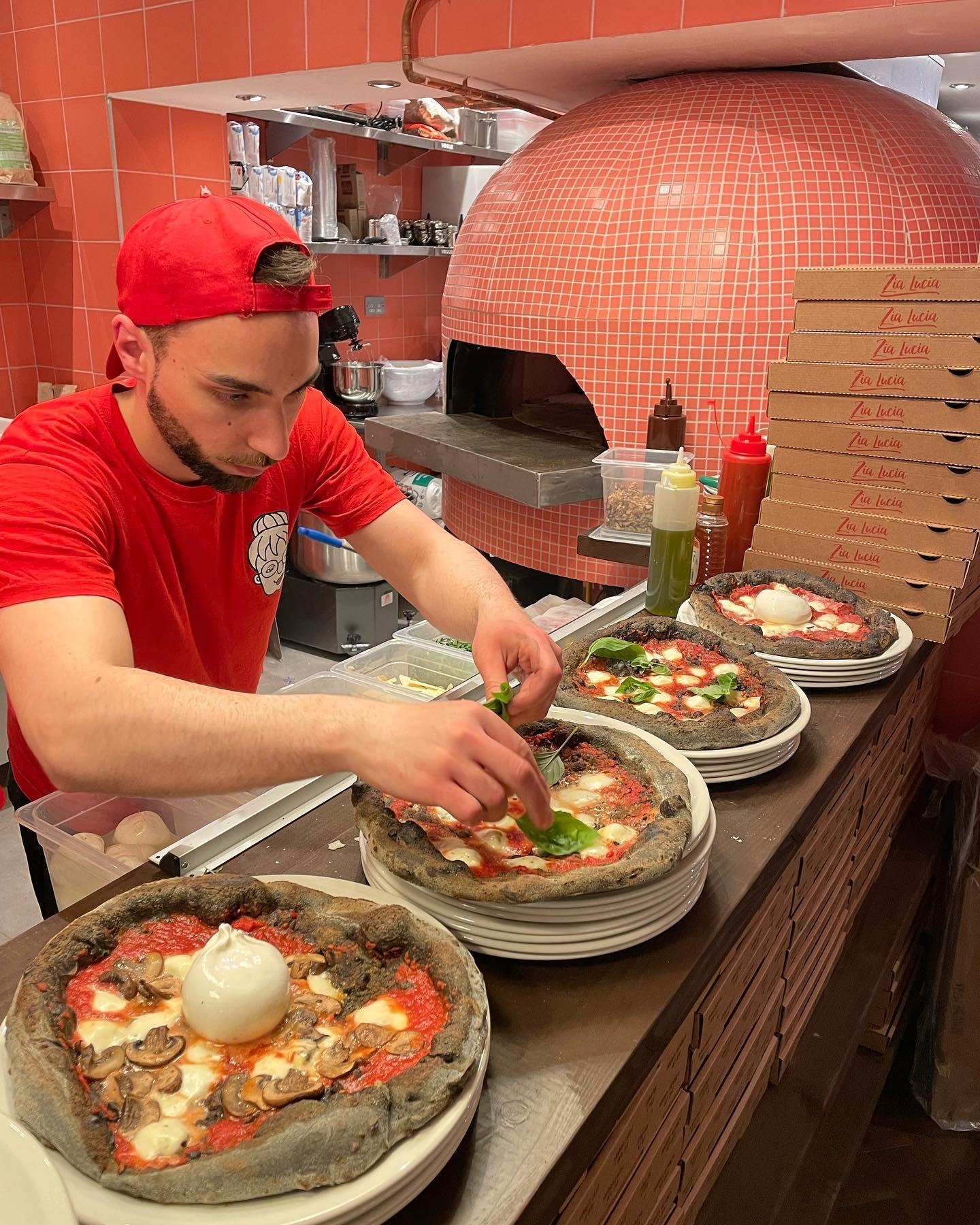 Chef at Zia Lucia putting the final ingredients onto 4 pizzas