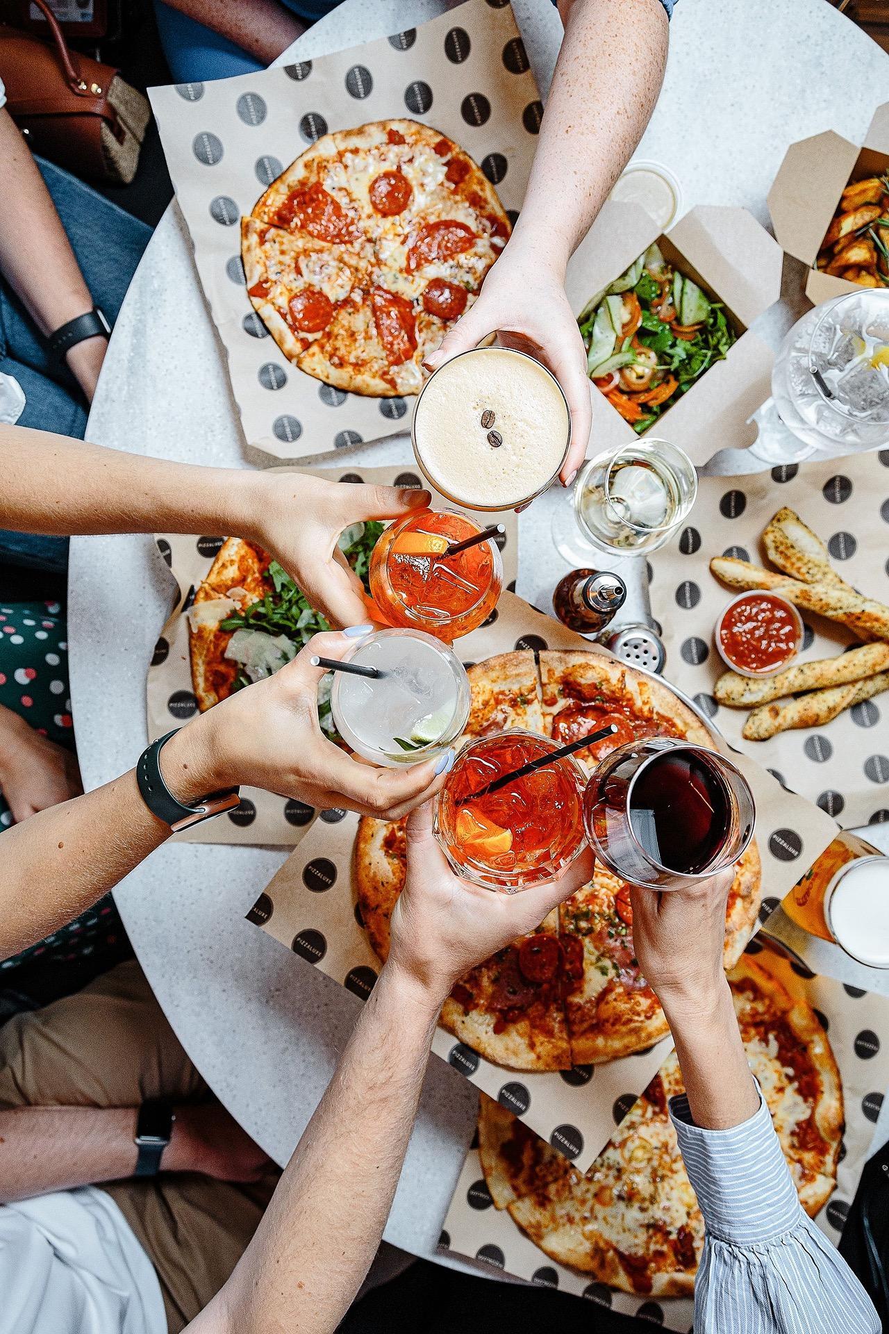 People toasting at a table full of pizza at pizzaluxe